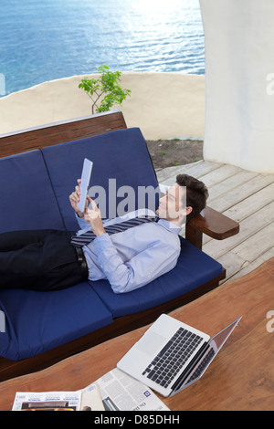 Businessman lying on soflooking tablette numérique. Banque D'Images