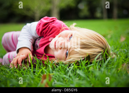 Petite fille toddler lying in grass in park smiling contact visuel Banque D'Images