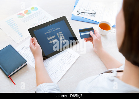 Femme d'entrer les informations de connexion pour effectuer l'opération bancaire en ligne sur tablette numérique dans l'office Banque D'Images