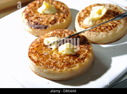 Répandre le beurre avec un couteau sur une chaude crumpet grillé pour le petit déjeuner ou le thé Banque D'Images