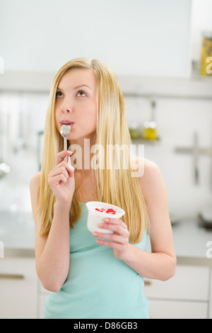 Adolescente réfléchie girl eating yogurt in kitchen Banque D'Images
