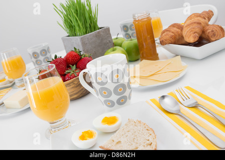 Petit-déjeuner savoureux et sain. Jus de fruits, oeufs, fruits, croissants, comfiture. Banque D'Images