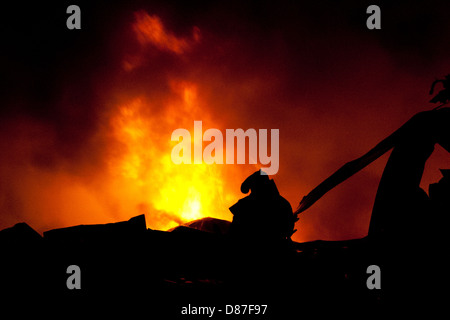 Silhouette de pompiers la lutte contre un feu faisant rage avec d'immenses flammes de bois brûlant Banque D'Images