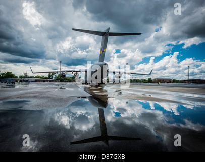 Le C-17 Globemaster III, un gros avion de transport militaire, se reflète dans une flaque d'eau de pluie, mettant en valeur son design élégant et sa taille impressionnante. Cet avion est crucial pour les missions de transport aérien lourd dans le monde entier. Banque D'Images