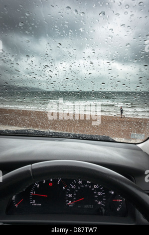 Pluie Royaume-Uni, plage de la côte sud à travers un pare-brise de voiture sur un jour de pluie au printemps / été avec un homme en cours d'exécution Banque D'Images