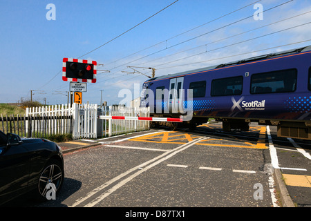 Train électrique traversant un passage contrôlé, montrant les feux de circulation et de contrôle barrière, Ayrshire, Scotland, UK Banque D'Images