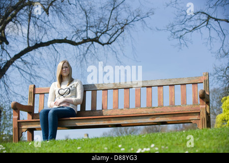 Une jeune femme assise sur un banc de parc par elle-même. Banque D'Images