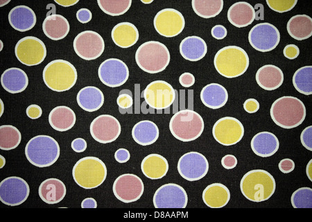 Une image en gros plan de tissu noir orné de points roses, violets et jaunes, mettant en valeur un motif ludique et vibrant. La texture du tissu ajoute de la profondeur et de l'intérêt visuel au design. Banque D'Images