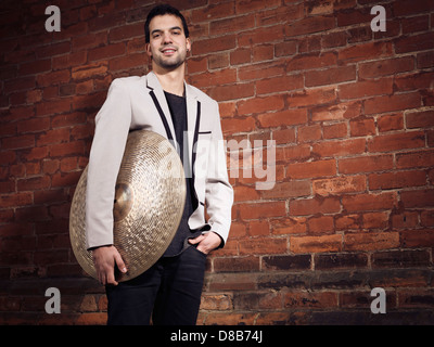 Portrait artistique d'un jeune homme tenant une musicial cymbale ride debout à un mur de briques Banque D'Images
