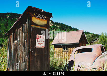 Old outhouse avec aucun stationnement et 'Shown uniquement sur rendez-vous' enseignes fixées, avec voiture rouillée abandonnée à proximité de Silver City, ID Banque D'Images