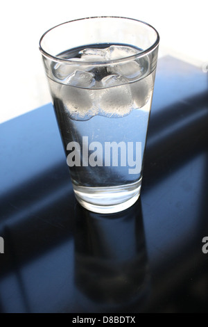 Un verre clair d'eau glacée placé sur un rebord de fenêtre, reflétant la lumière qui pénètre à travers la fenêtre. L'image met en valeur la simplicité et la fraîcheur. Banque D'Images