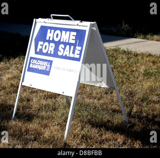 Panneau indiquant une maison à vendre, placé devant une propriété résidentielle. Le signe est bien visible dans la cour avant, signalant la disponibilité de la maison à l'achat. Banque D'Images
