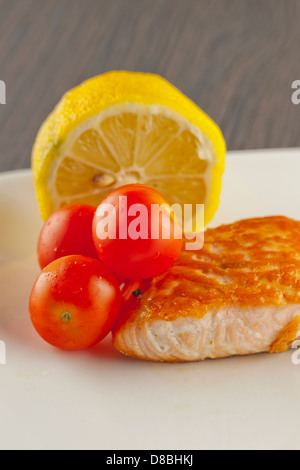 Morceau de salmon sur une plaque blanche, avec des tomates et citron Banque D'Images