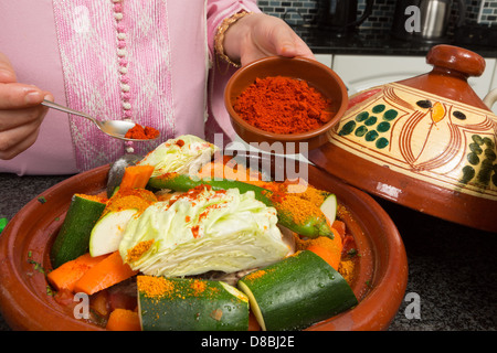 La femme immigrante marocaine traditionnelle en Europe l'ajout d'épices à tajine son pendant le Ramadan dans sa cuisine moderne Banque D'Images