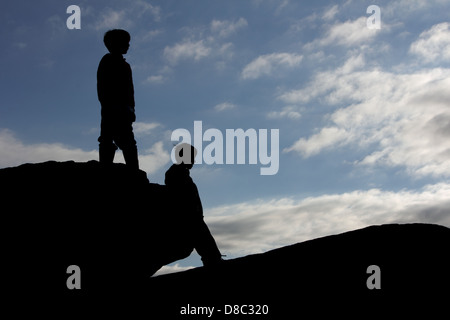 Deux jeunes garçons en silhouette debout sur deux rochers à la recherche dans la distance Banque D'Images