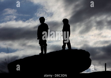 Deux jeunes garçons en silhouette debout sur un rocher à la recherche dans la distance Banque D'Images