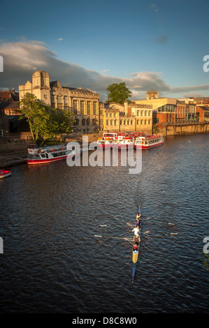 Une flotte de bateaux de croisière et de bateaux touristiques amarrés le long du Guildhall lors d'une soirée d'été ensoleillée avec un bateau à rames au premier plan.River Ouse, York. Banque D'Images