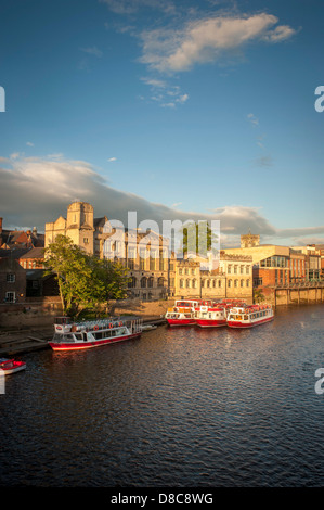 River Ouse avec une flotte de bateaux de croisière et de location de touristes amarrés le long du Guildhall lors d'une soirée d'été ensoleillée à York. Banque D'Images