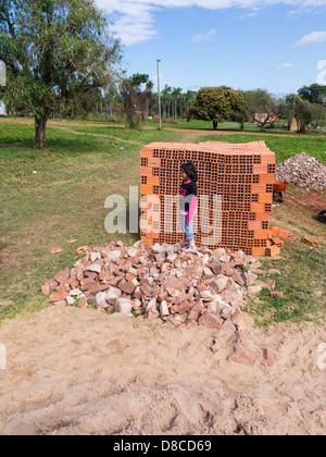 Une jeune fille hispanique s'élève face à une pile de blocs de construction en céramique pour la construction domiciliaire dans un bâtiment d'accueil du site. Banque D'Images