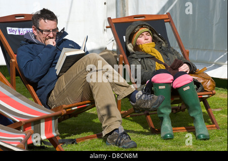 Les visiteurs à lire et dormir assis au soleil assis dans des transats mais enveloppé contre le vent froid à Hay Festival Hay-on-Wye Banque D'Images