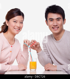 Jeune couple partage d'un verre de jus d'orange, studio shot Banque D'Images