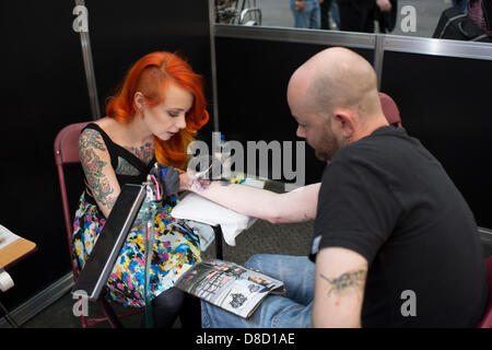 Modèle US et tatoueur, Megan Massacre de New York, travaille sur un homme à la Great British Tattoo Show, London, UK. Banque D'Images