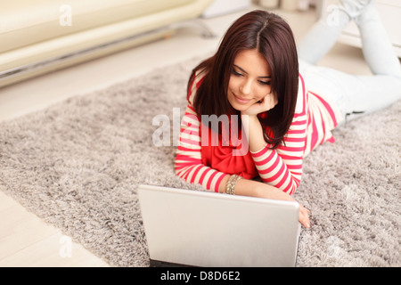 Portrait de jeune femme rêveuse using laptop while lying on floor at home Banque D'Images