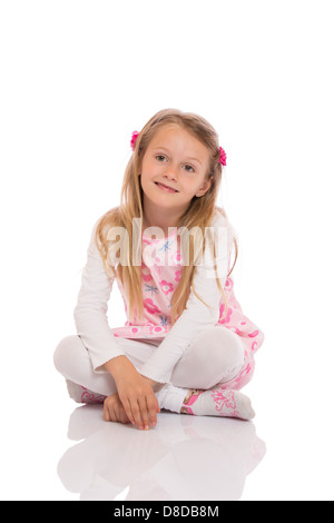 Portrait d'une petite fille aux cheveux longs assis les jambes croisées sur le plancher et de sourire. Banque D'Images