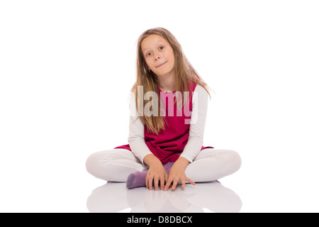 Portrait d'une jeune fille aux cheveux longs assis les jambes croisées sur le plancher et faire des grimaces. Isolé sur fond blanc. Banque D'Images