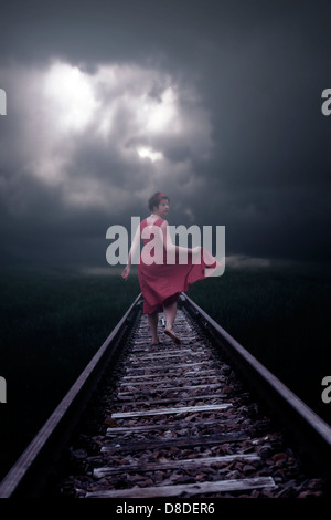 Une fille dans une robe rouge est en cours d'exécution sur des rails de chemin de fer Banque D'Images