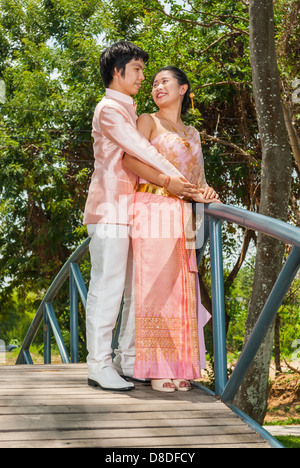 Thai asiatique suite nuptiale en costume de mariage thaï est debout à regarder les uns les autres à côté de blue bridge. Banque D'Images