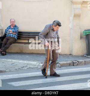 Homme âgé traverse zebra crossing à l'aide d'un bâton de marche Banque D'Images