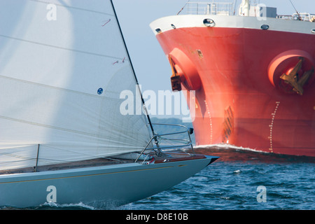 La proue d'un grand cargo qui pousse dans l'eau et traverse un bateau à voile dans la baie de Narragansett dans Rhode Island Banque D'Images