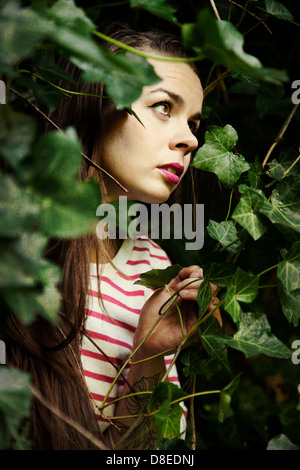 Woman Peering à travers vignes luxuriantes Banque D'Images