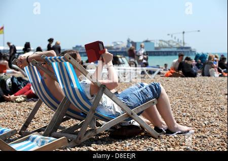 Femme se lit à l'aide d'un appareil électronique kindle comme le front de mer et la plage ont été emballés à Brighton aujourd'hui comme la foule profiter du beau temps de la banque Banque D'Images