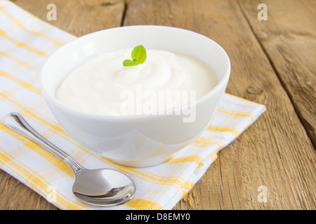 Yogourt nature blanc frais dans un bol avec la menthe et déposer sur fond de bois rustique (tableau) close up, copy space Banque D'Images