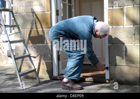 75 ans de peinture pensionné le porche de sa maison à North Yorkshire, England, UK Banque D'Images