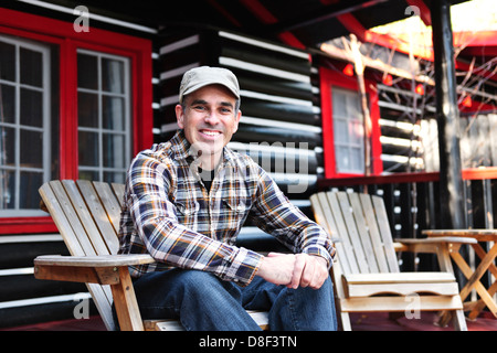 Smiling man sitting on deck en bois chalet en chaise adirondack Banque D'Images