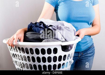 Habillé en passant la femme en bleu shirt tenant un panier plein de linge sale ayant besoin de lave Banque D'Images