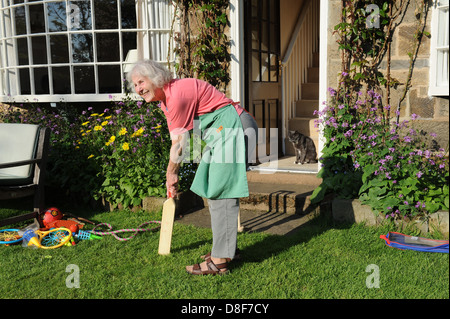 Grand-mère âgée de jouer à un jeu de cricket dans le jardin de la maison de sa famille dans le Yorkshire du Nord. Banque D'Images