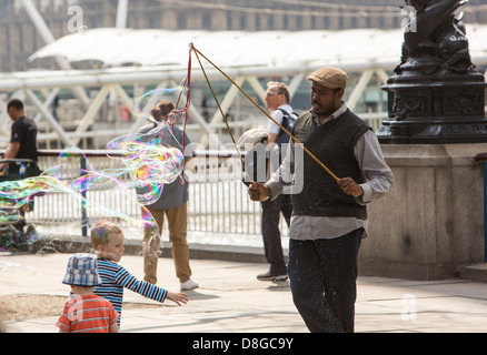 Les enfants bulles chasse faite par un artiste de rue sur la rive sud de Londres. Banque D'Images