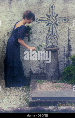 Une femme en deuil avec voile et robe sombre sur un cimetière, placer des fleurs sur une tombe Banque D'Images