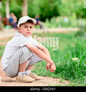 Portrait of boy sitting in a park squat Banque D'Images