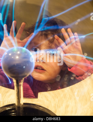 Petite fille touche une boule de plasma avec ses mains et regarde la décharge électrostatique Banque D'Images