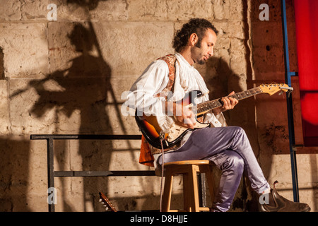 Jérusalem, Israël. Un homme joue d'une guitare électrique. L'ombre d'un flûtiste apparaît sur les murs de la vieille ville derrière lui. Banque D'Images