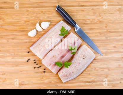 Photo horizontale de filets de poisson blanc, couteau, persil, ail et poivre de voirie sur fond de bois de bambou naturel Banque D'Images