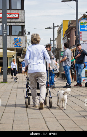 Caucasian woman with gris, cheveux gris poussant un bébé buggy, marchant vers un arrêt de bus dans la ville - Heilbronn, Allemagne Banque D'Images