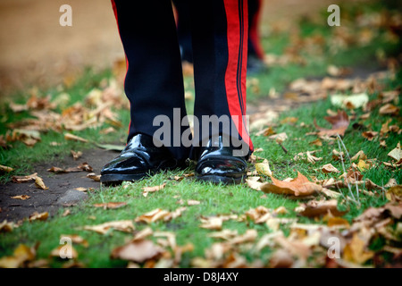 Les jambes d'un soldat en uniforme avec des chaussures noires brillantes, debout sur l'herbe avec brown feuilles d'automne Banque D'Images