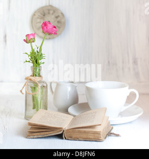 Fleurs roses remorquage ranunculus dans old vintage bouteille, ancienne bibliothèque d'ouverture et une tasse de thé sur la table en bois blanc Banque D'Images