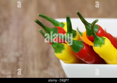 Piments rouges et jaunes dans un bol blanc sur fond de bois with copy space Banque D'Images